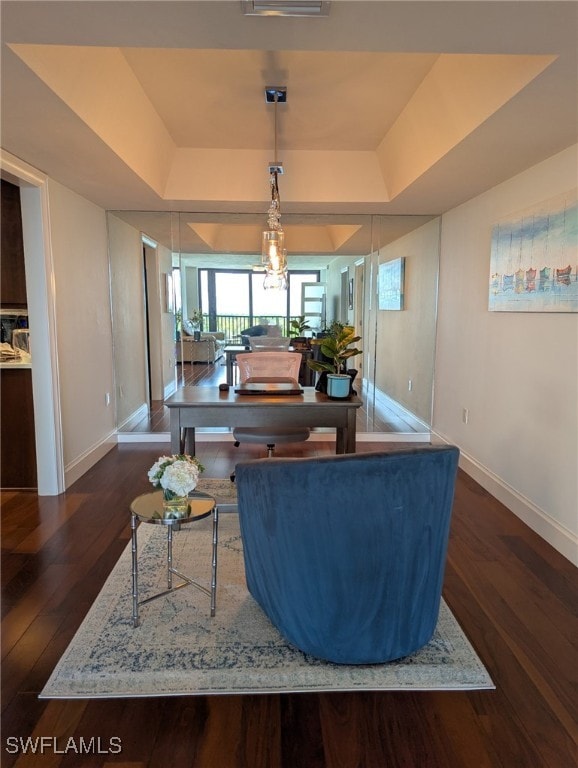 living area featuring baseboards, a tray ceiling, and wood finished floors