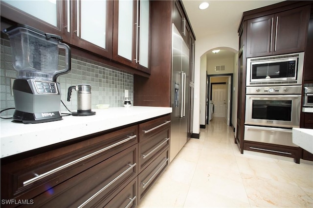 kitchen featuring backsplash, dark brown cabinetry, light tile patterned floors, and stainless steel appliances