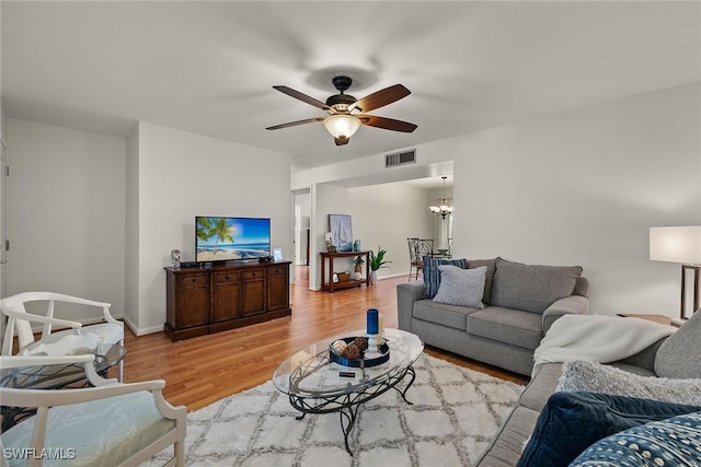 living room featuring ceiling fan with notable chandelier and light hardwood / wood-style flooring