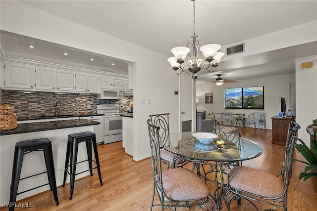 dining space with ceiling fan with notable chandelier, light wood-type flooring, and sink