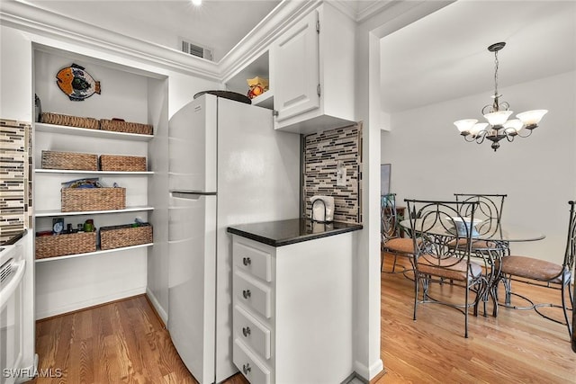 kitchen with light wood-type flooring, backsplash, a chandelier, white fridge, and white cabinetry