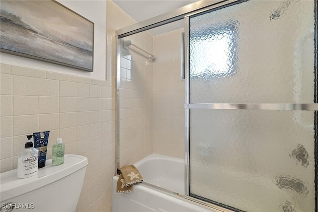 bathroom featuring shower / bath combination with glass door, toilet, and tile walls