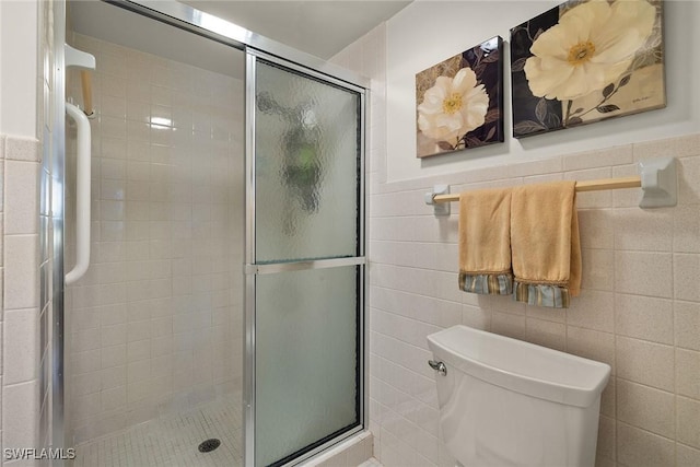 bathroom featuring toilet, tile walls, and a shower with shower door