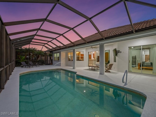 pool at dusk with a lanai, ceiling fan, and a patio