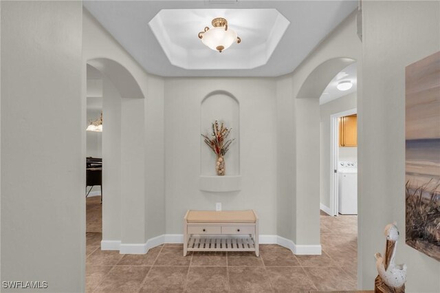 corridor with a raised ceiling, washer / clothes dryer, and tile patterned flooring