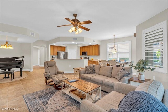 tiled living room with ceiling fan with notable chandelier