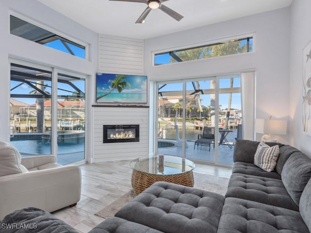 living room with a fireplace, a towering ceiling, light hardwood / wood-style floors, and ceiling fan