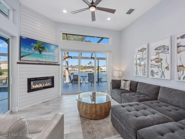 living room featuring ceiling fan, a towering ceiling, and a fireplace