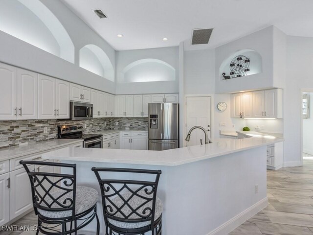 kitchen with white cabinets, a kitchen breakfast bar, a towering ceiling, and appliances with stainless steel finishes