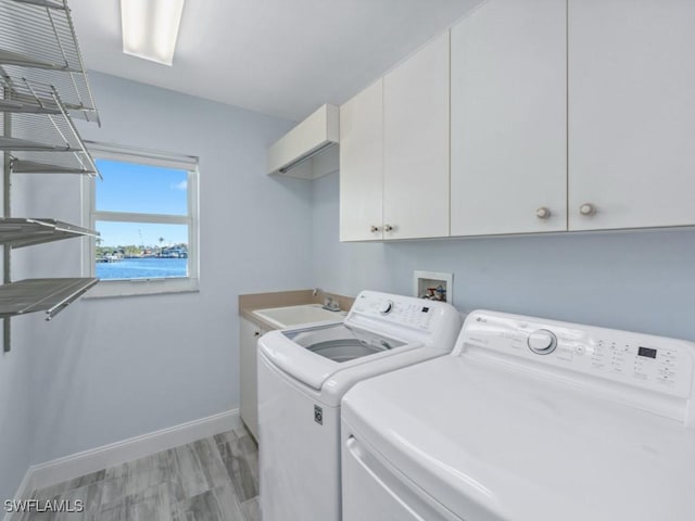 clothes washing area featuring cabinets, a water view, sink, light hardwood / wood-style flooring, and washing machine and clothes dryer