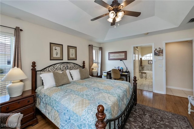 bedroom with ensuite bathroom, wood-type flooring, ceiling fan, and a tray ceiling