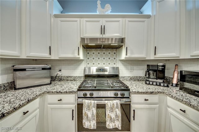 kitchen with under cabinet range hood, stainless steel gas range oven, white cabinetry, and decorative backsplash