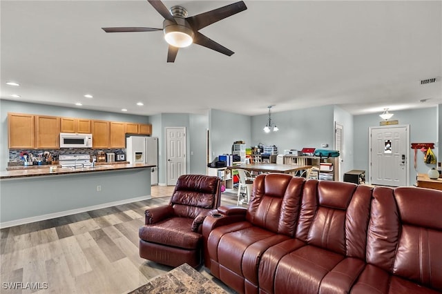 living room featuring ceiling fan with notable chandelier, light hardwood / wood-style floors, and sink