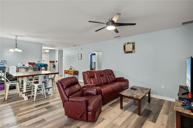 living room featuring ceiling fan with notable chandelier and light wood-type flooring