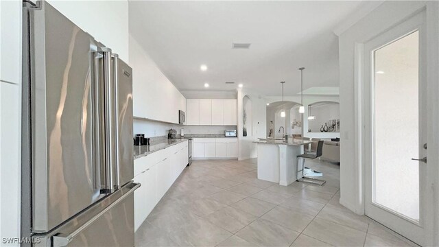 kitchen with appliances with stainless steel finishes, hanging light fixtures, an island with sink, a breakfast bar, and white cabinets