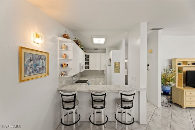 kitchen featuring white cabinetry, light stone counters, kitchen peninsula, white appliances, and a breakfast bar area