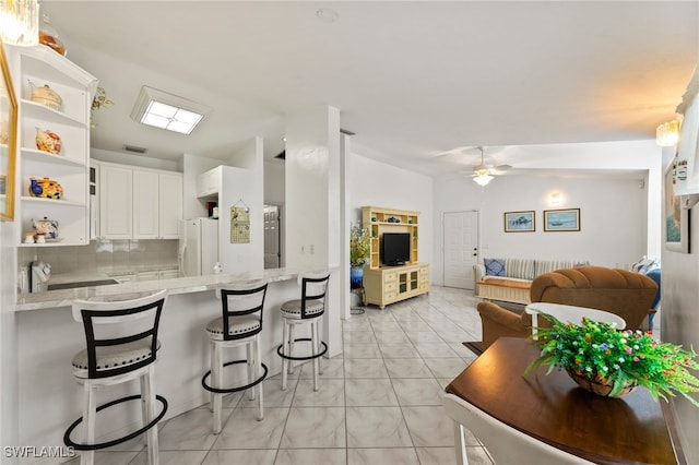 kitchen featuring ceiling fan, kitchen peninsula, a breakfast bar area, decorative backsplash, and white cabinets