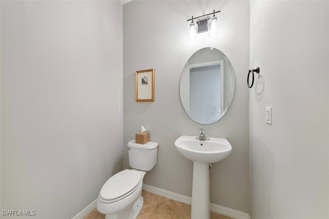 half bathroom with a sink, baseboards, toilet, and tile patterned flooring