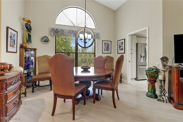 dining area with light hardwood / wood-style floors, a high ceiling, and a chandelier