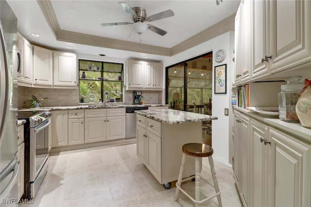 kitchen featuring ceiling fan, a center island, a kitchen bar, a tray ceiling, and stainless steel appliances