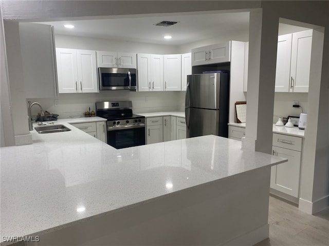 kitchen with kitchen peninsula, sink, stainless steel appliances, and white cabinetry