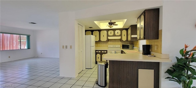 kitchen featuring dark brown cabinetry, white refrigerator, backsplash, kitchen peninsula, and stove