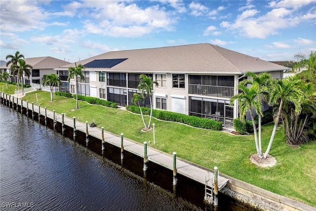 back of house with a sunroom, a water view, and a lawn