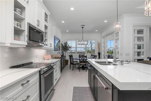 kitchen featuring crown molding, a chandelier, decorative backsplash, stainless steel appliances, and a sink