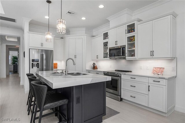 kitchen featuring a center island with sink, sink, hanging light fixtures, light stone counters, and stainless steel appliances