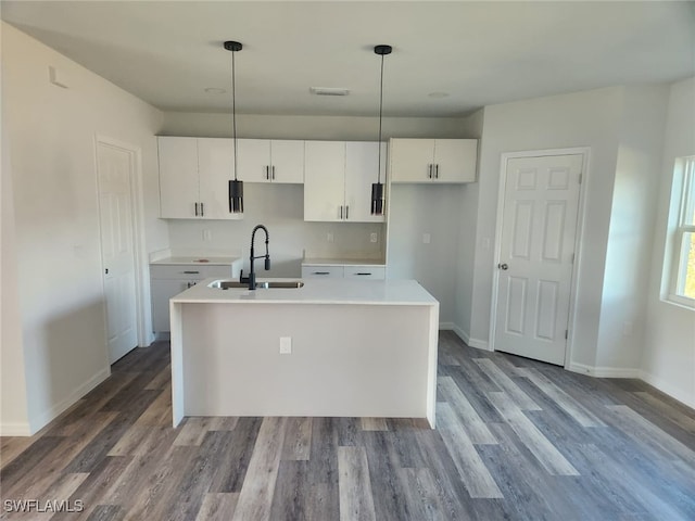 kitchen with decorative light fixtures, sink, white cabinetry, and an island with sink