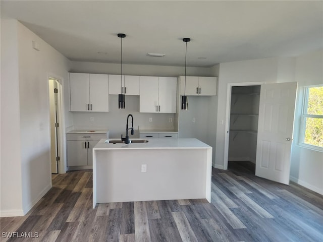 kitchen featuring white cabinetry, sink, hanging light fixtures, dark hardwood / wood-style flooring, and a kitchen island with sink