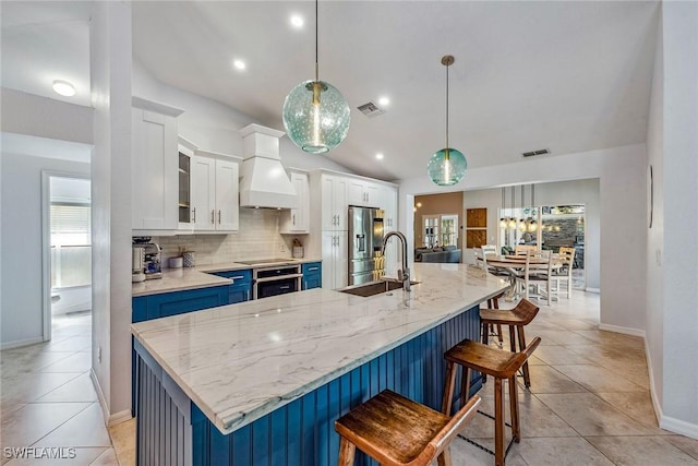 kitchen with a large island with sink, blue cabinets, sink, decorative light fixtures, and white cabinetry