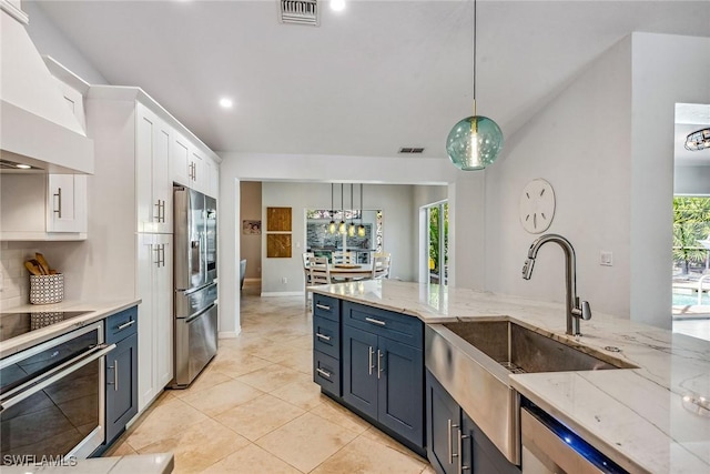 kitchen with appliances with stainless steel finishes, premium range hood, blue cabinetry, white cabinetry, and hanging light fixtures