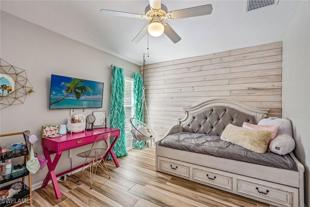 bedroom with ceiling fan, wood walls, and light wood-type flooring