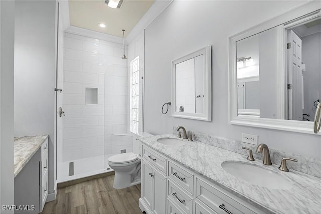 bathroom with double vanity, wood finished floors, a tile shower, and a sink