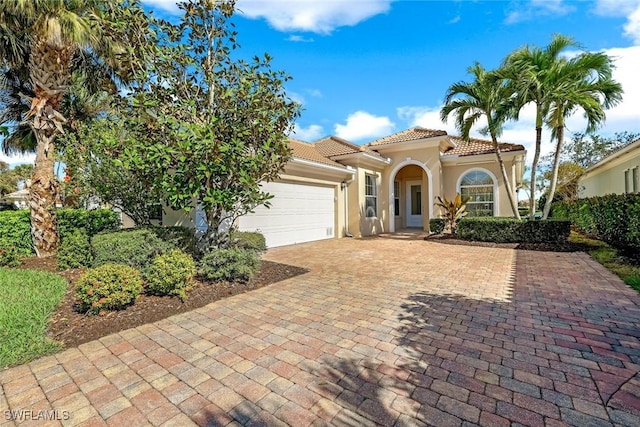 mediterranean / spanish-style home featuring stucco siding, an attached garage, a tile roof, and decorative driveway