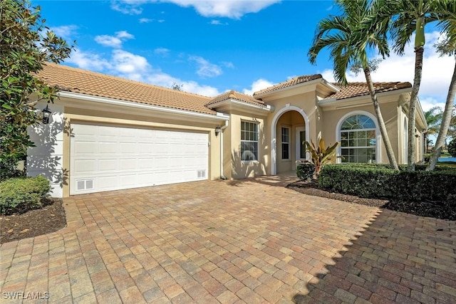 mediterranean / spanish-style home with a tile roof, decorative driveway, a garage, and stucco siding