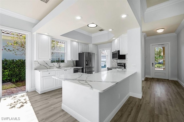 kitchen with ornamental molding, light stone counters, white cabinets, stainless steel appliances, and a sink