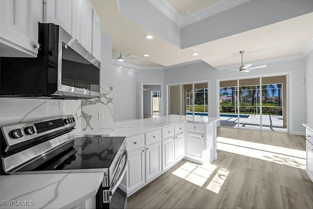 kitchen featuring light wood-style flooring, appliances with stainless steel finishes, a peninsula, crown molding, and white cabinets