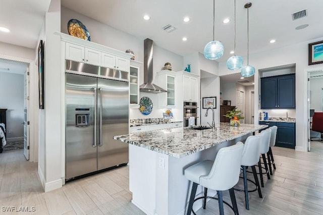 kitchen with decorative light fixtures, white cabinetry, stainless steel appliances, blue cabinetry, and wall chimney range hood