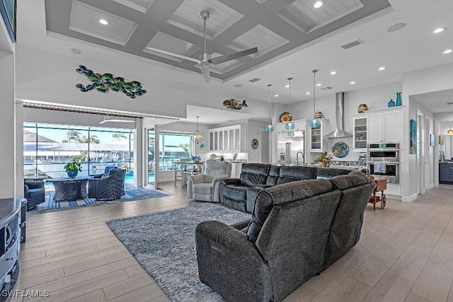 living room featuring coffered ceiling, light wood-type flooring, ceiling fan, beam ceiling, and a high ceiling