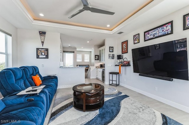 living room with ornamental molding, light wood-type flooring, ceiling fan, and a tray ceiling