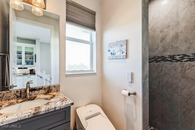 bathroom with vanity, plenty of natural light, a tile shower, and toilet