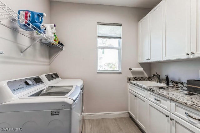 clothes washing area featuring cabinets, separate washer and dryer, sink, and light hardwood / wood-style floors