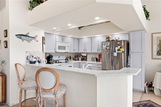 kitchen featuring a breakfast bar, white appliances, sink, light tile patterned floors, and kitchen peninsula