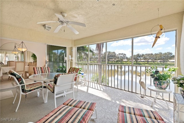 sunroom with ceiling fan and a water view