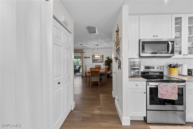 kitchen featuring pendant lighting, backsplash, light wood-type flooring, white cabinetry, and stainless steel appliances