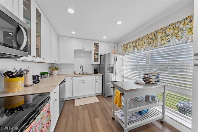 kitchen featuring sink, light stone countertops, appliances with stainless steel finishes, light hardwood / wood-style floors, and white cabinetry