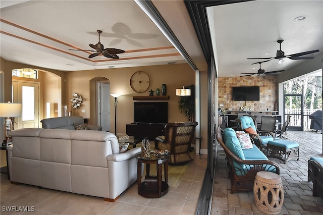 living room featuring ceiling fan, a raised ceiling, a fireplace, and tile patterned flooring