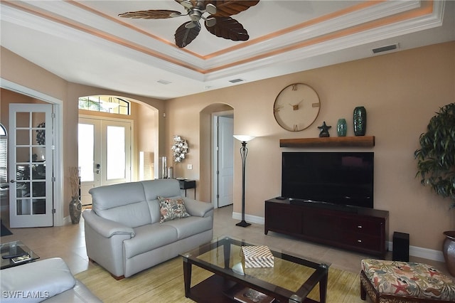 living room with french doors, a raised ceiling, ornamental molding, light tile patterned flooring, and ceiling fan